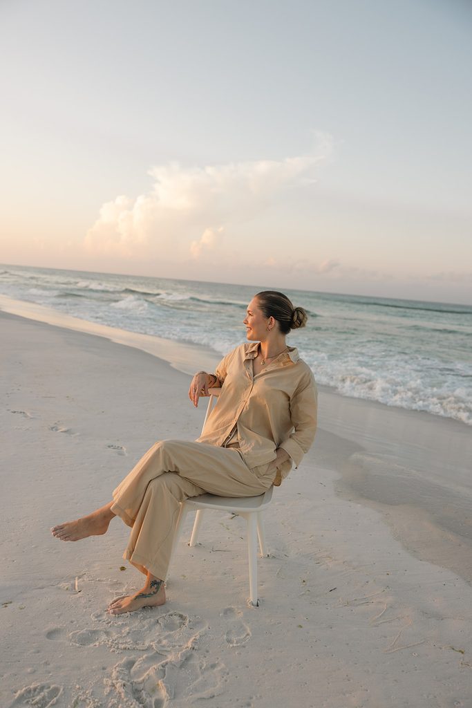 Alyssa, founder of HolSol, sitting in a chair at the beach during sunset